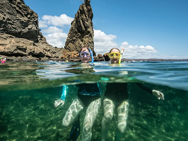 Snorkelers exploring the clear waters around Bartolome Island, Galapagos, with striking volcanic rock formations.